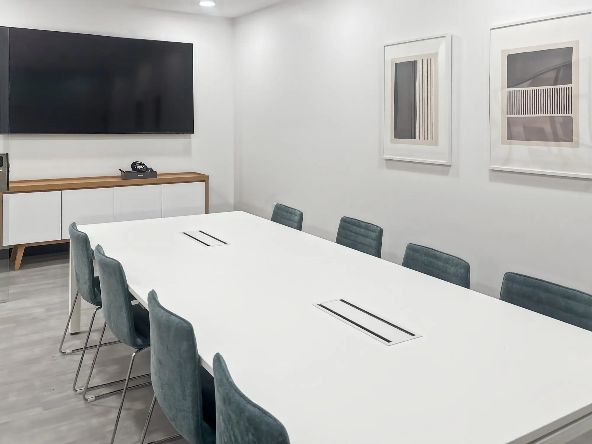 A boardroom with a long white table, teal chairs and a wall-mounted screen