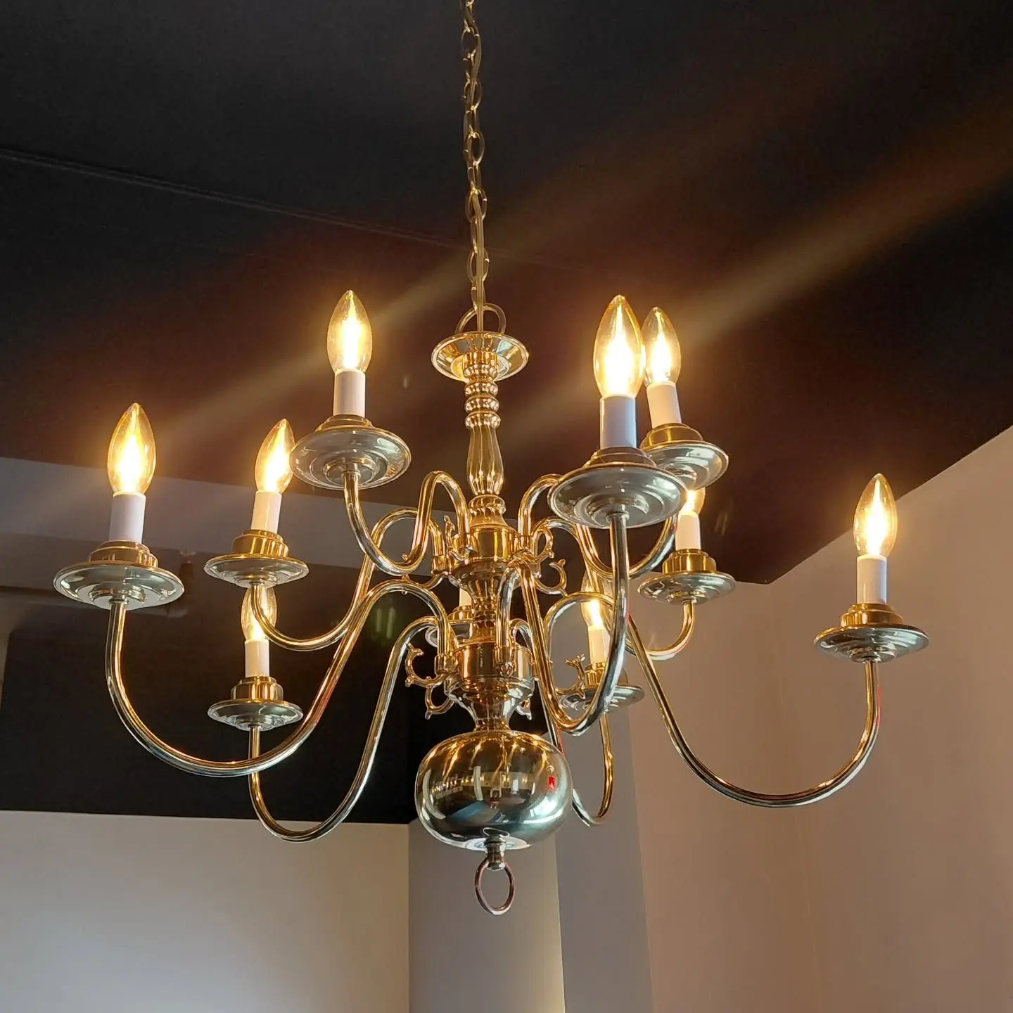 A brass candle chandelier glowing against a dark ceiling
