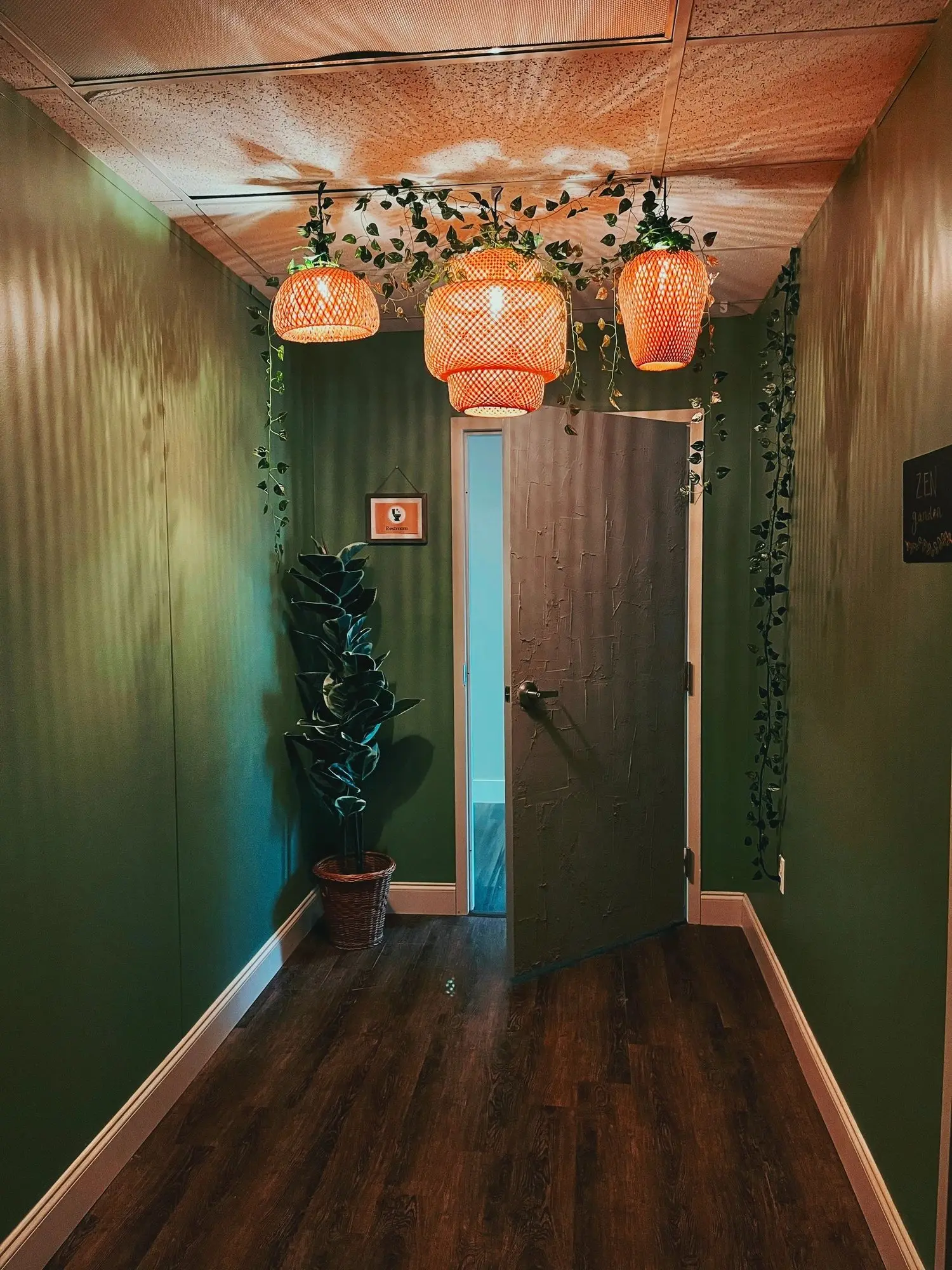 A green hallway hung with woven pendant lights and trailing greenery