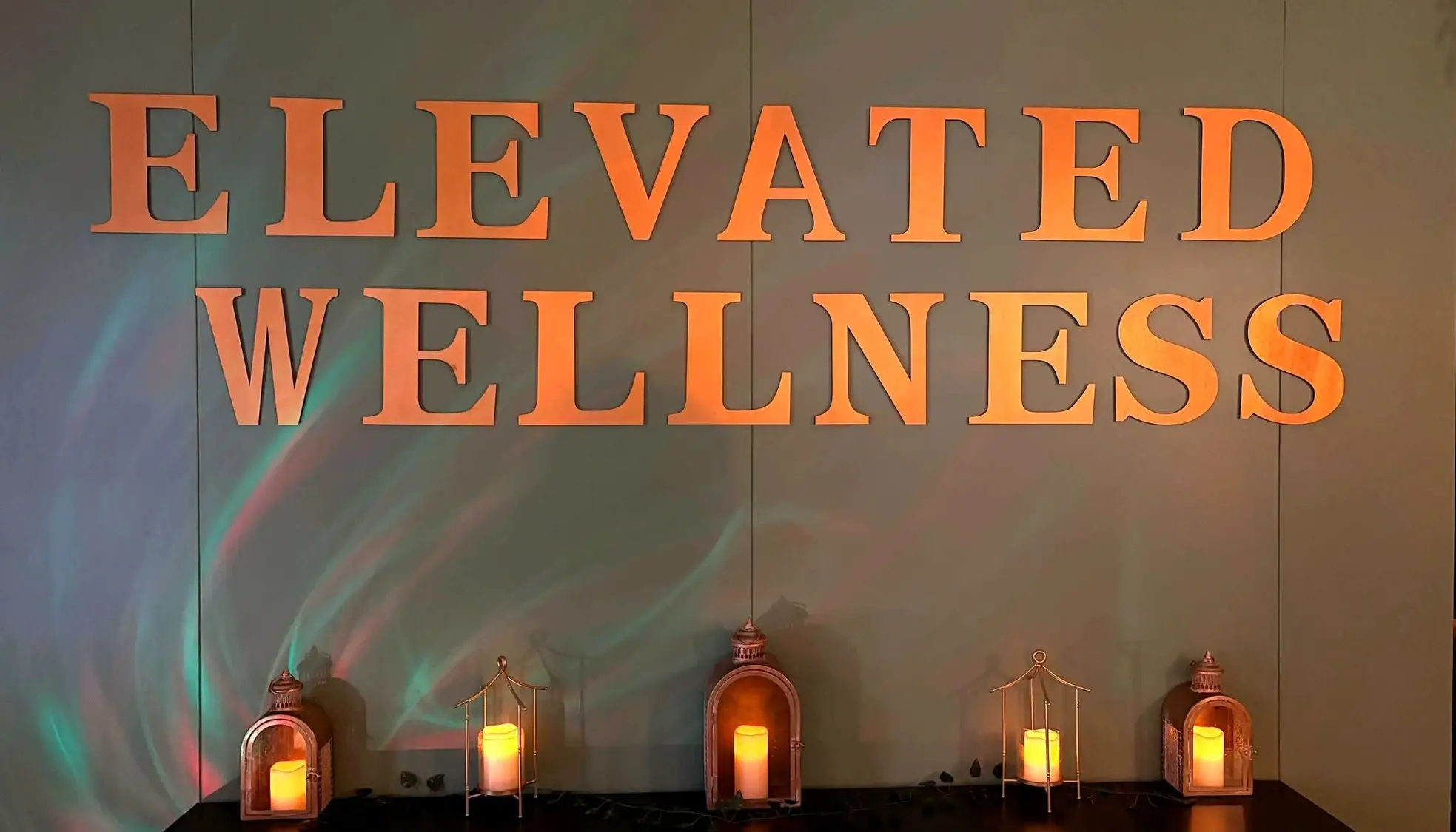 Gold Elevated Wellness lettering on a wall above a row of candle lanterns