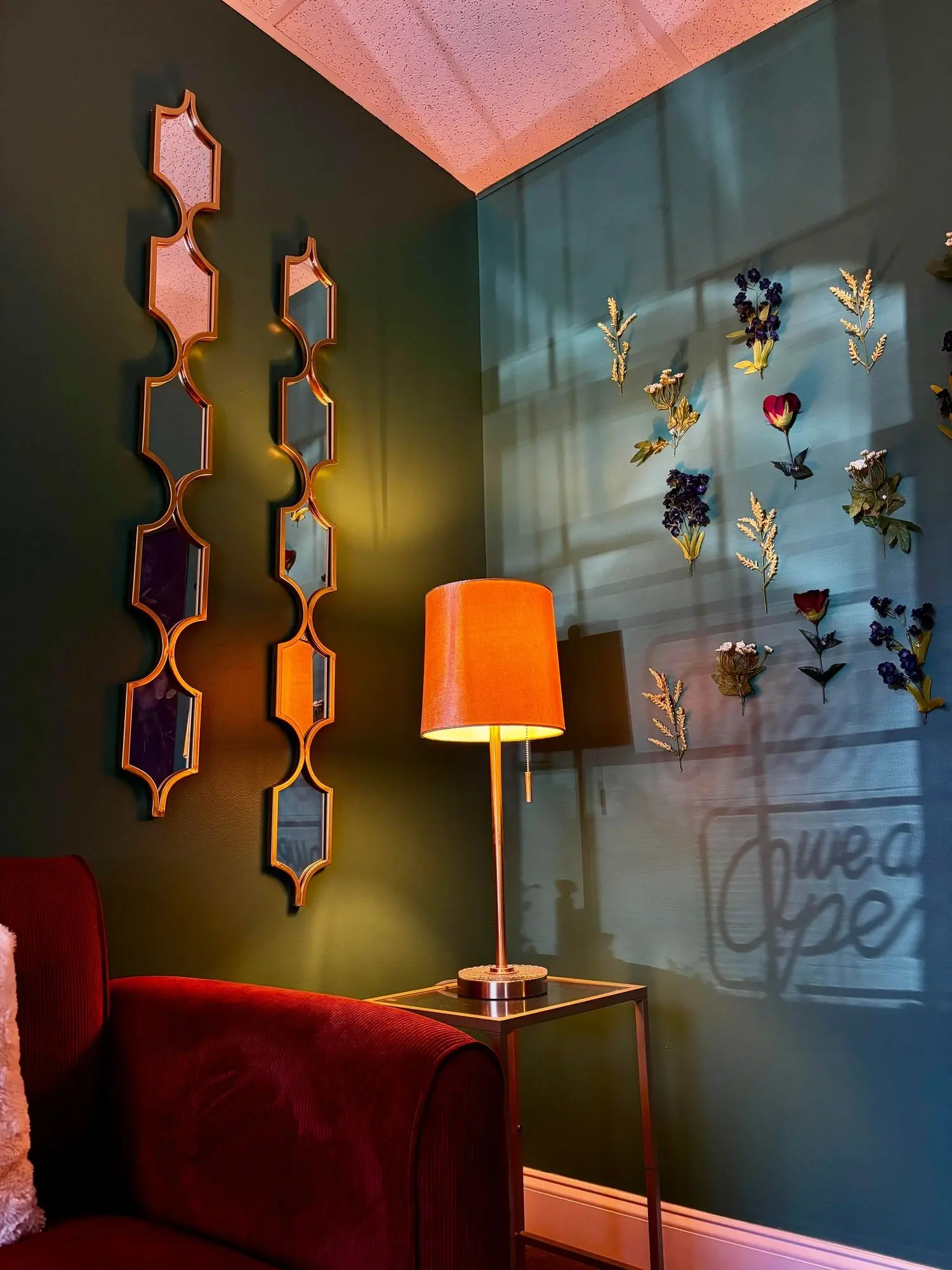A corner of the teal lobby with gold mirrors, a lamp and a red velvet chair