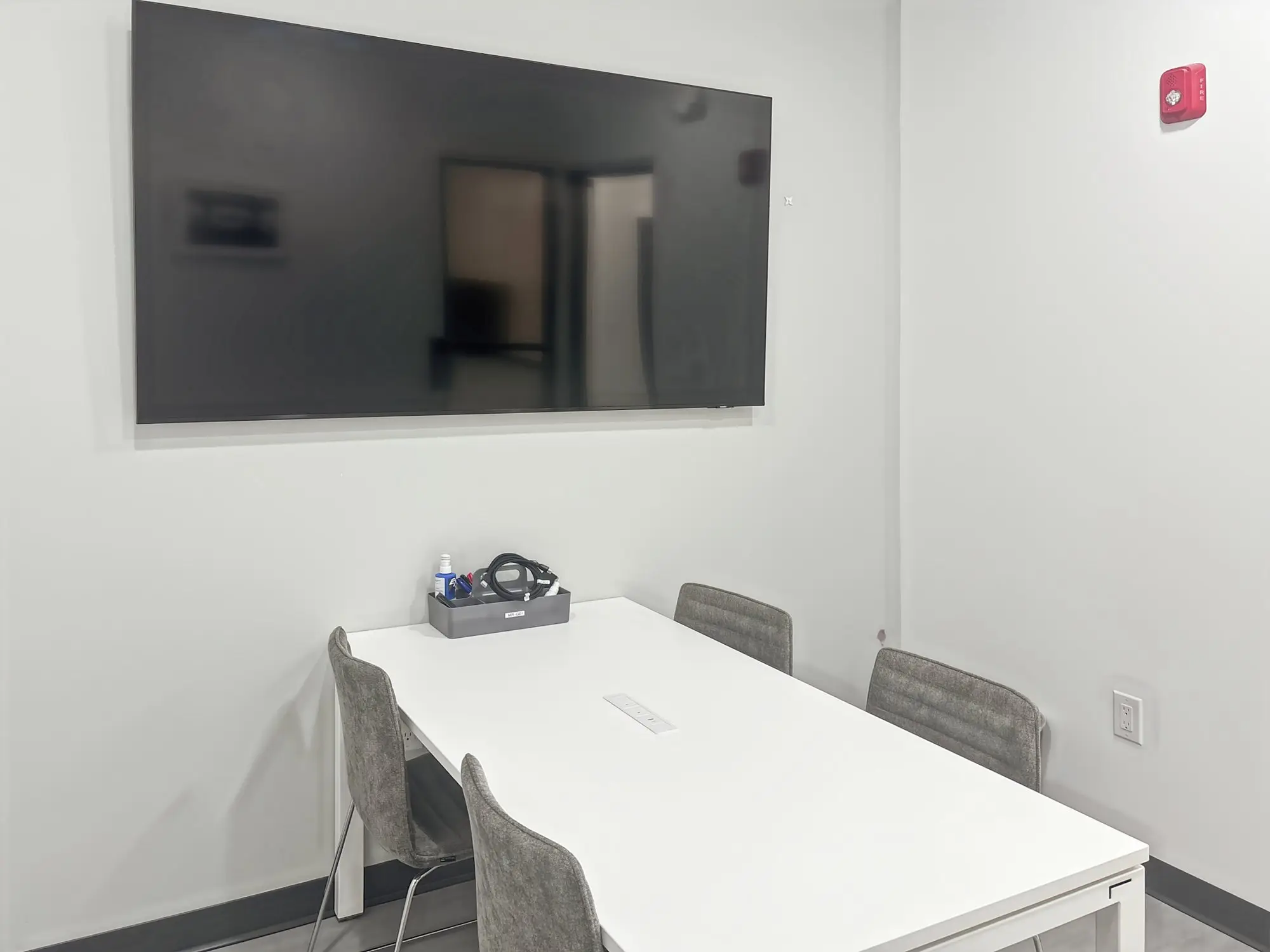 A small meeting room with a table for four and a large wall-mounted screen